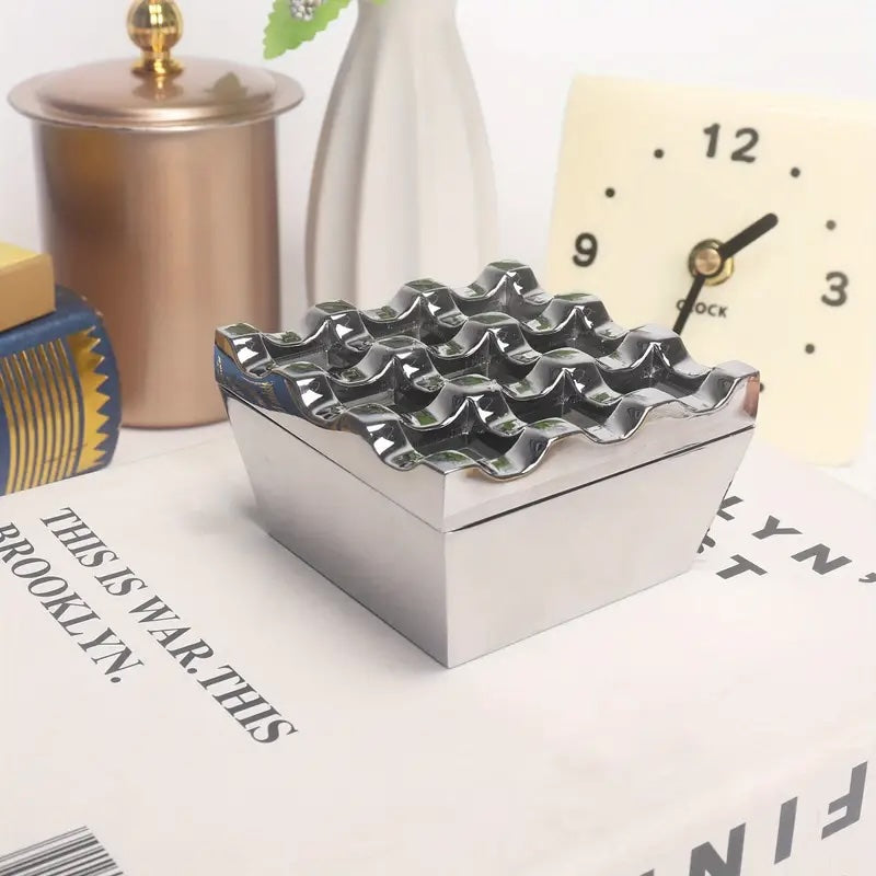 Metallic waffle iron on a surface with a clock and other items in the background
