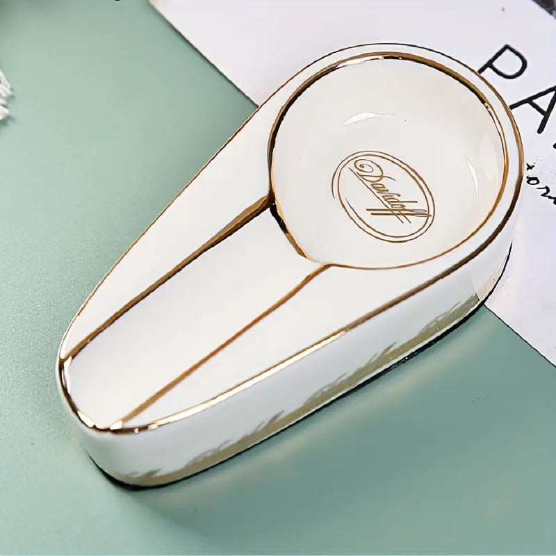 White and gold ceramic dish with a brand logo on a light green surface