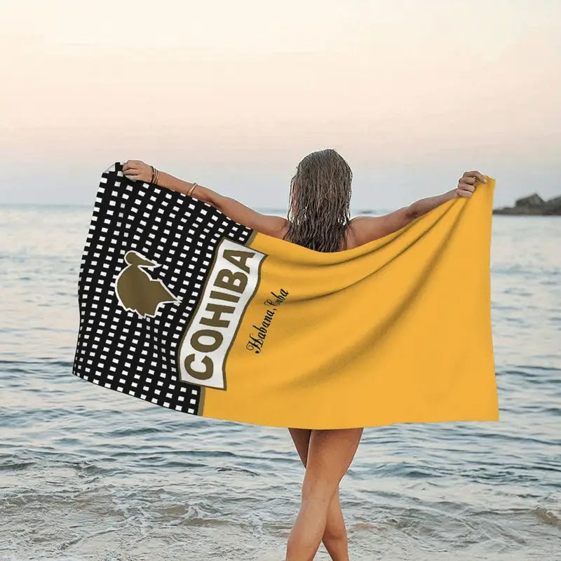 Person holding a large towel with Cohiba logo on a beach
